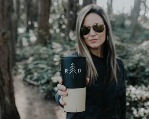 woman holding out cup of coffee while on a hike